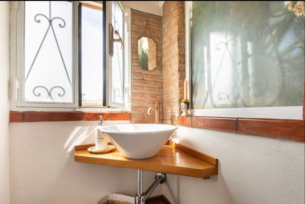 Bagno luminoso con lavandino moderno, finestra aperta e pareti in mattoni, Casa Vacanze Suvereto.