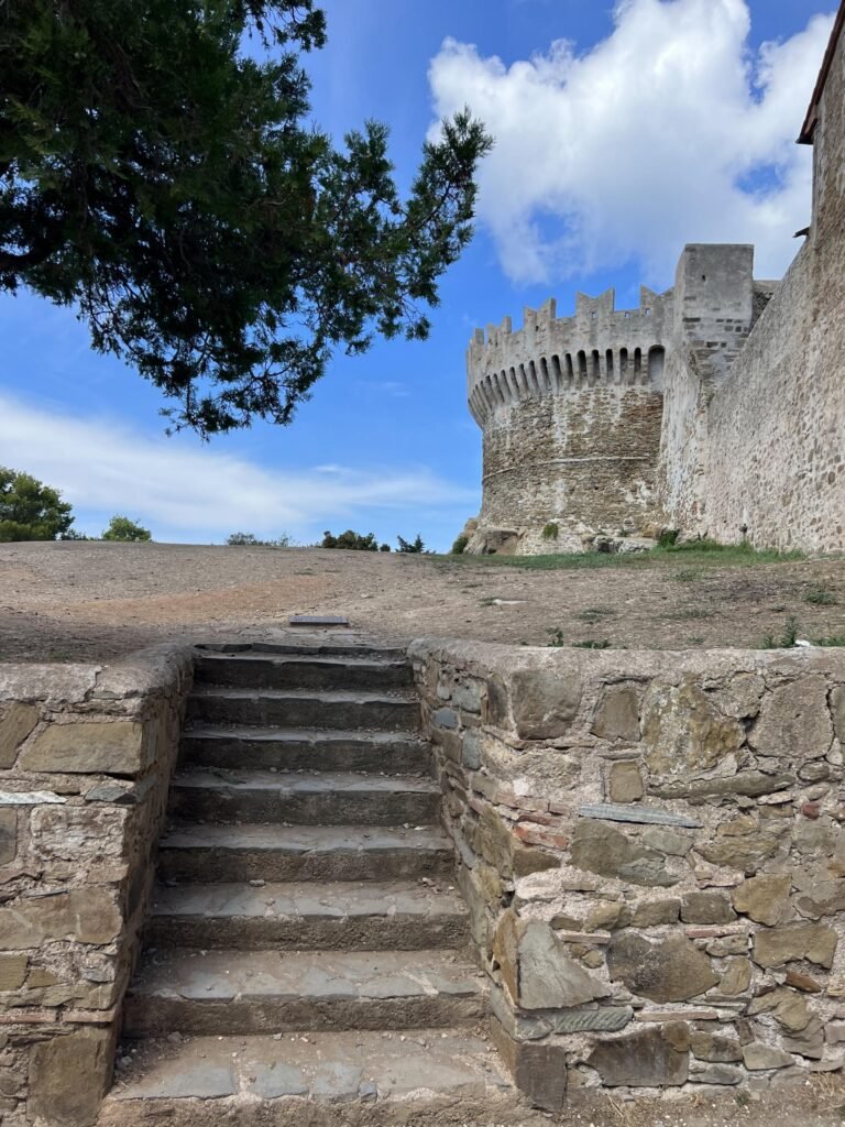 Scala verso la storica fortezza di Populonia, su uno sfondo di cielo azzurro e nuvole.