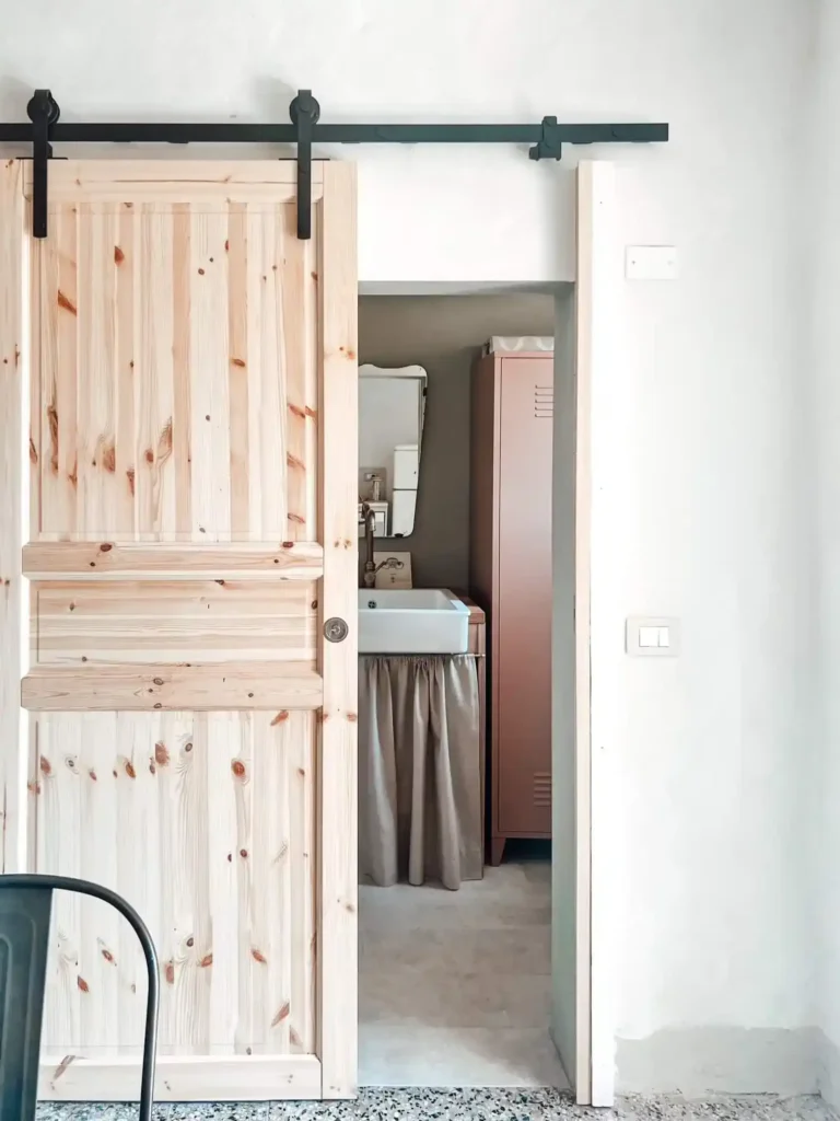 Porta scorrevole in legno in casa vacanze a Suvereto, ingresso bagno arredato in stile rustico accogliente.