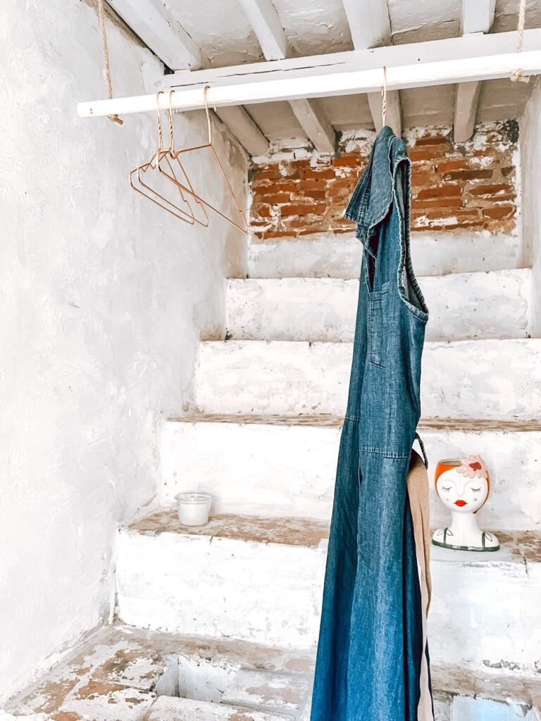 Abito di jeans appeso su scala rustica in casa vacanze a Suvereto, decorazione vintage e candele aggiungono fascino.