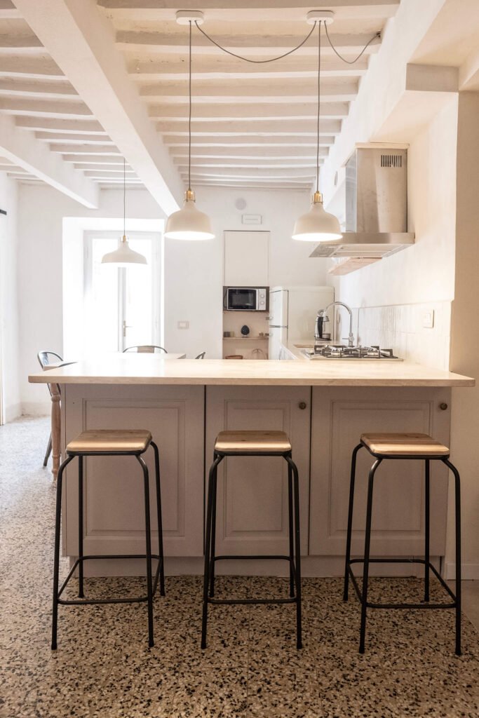 Cucina moderna con tre sgabelli, illuminazione pendente, e arredi eleganti nella casa vacanze Suvereto.
