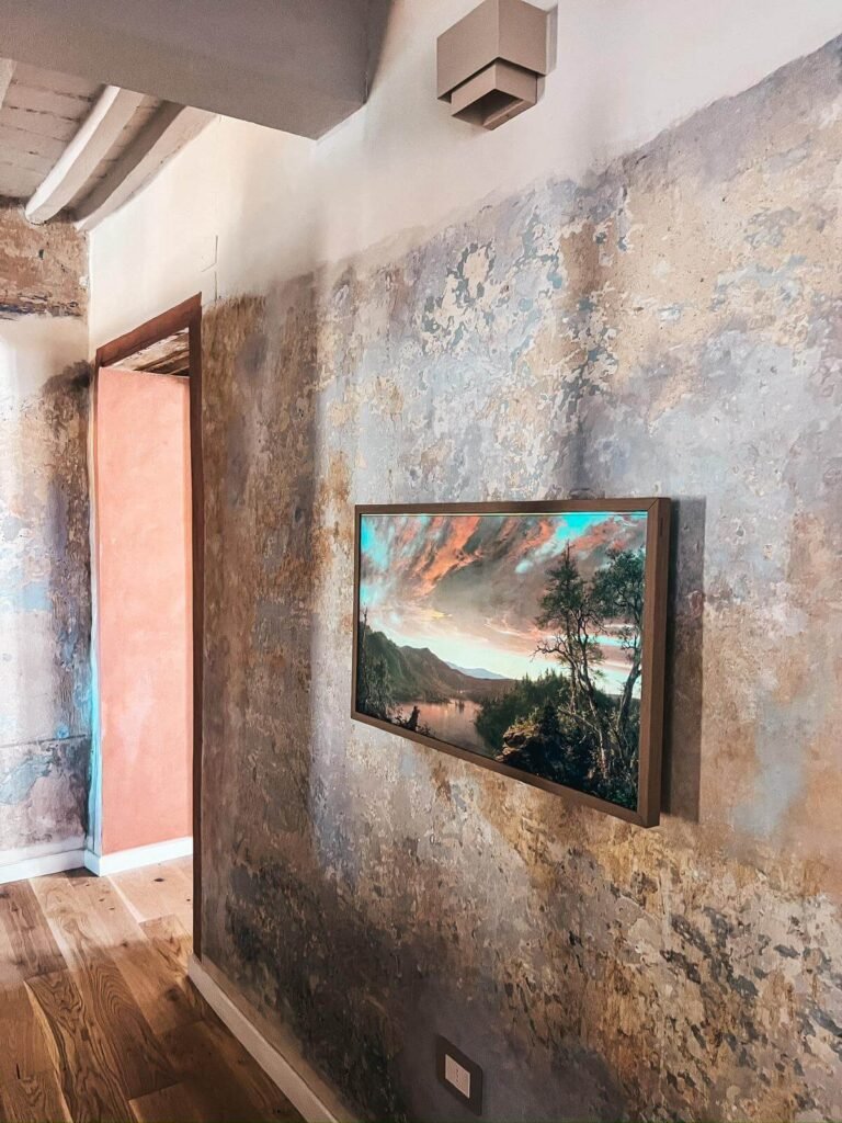 Interno rustico casa vacanze Suvereto, parete dipinta, finestra con vista, atmosfera accogliente e artistica.